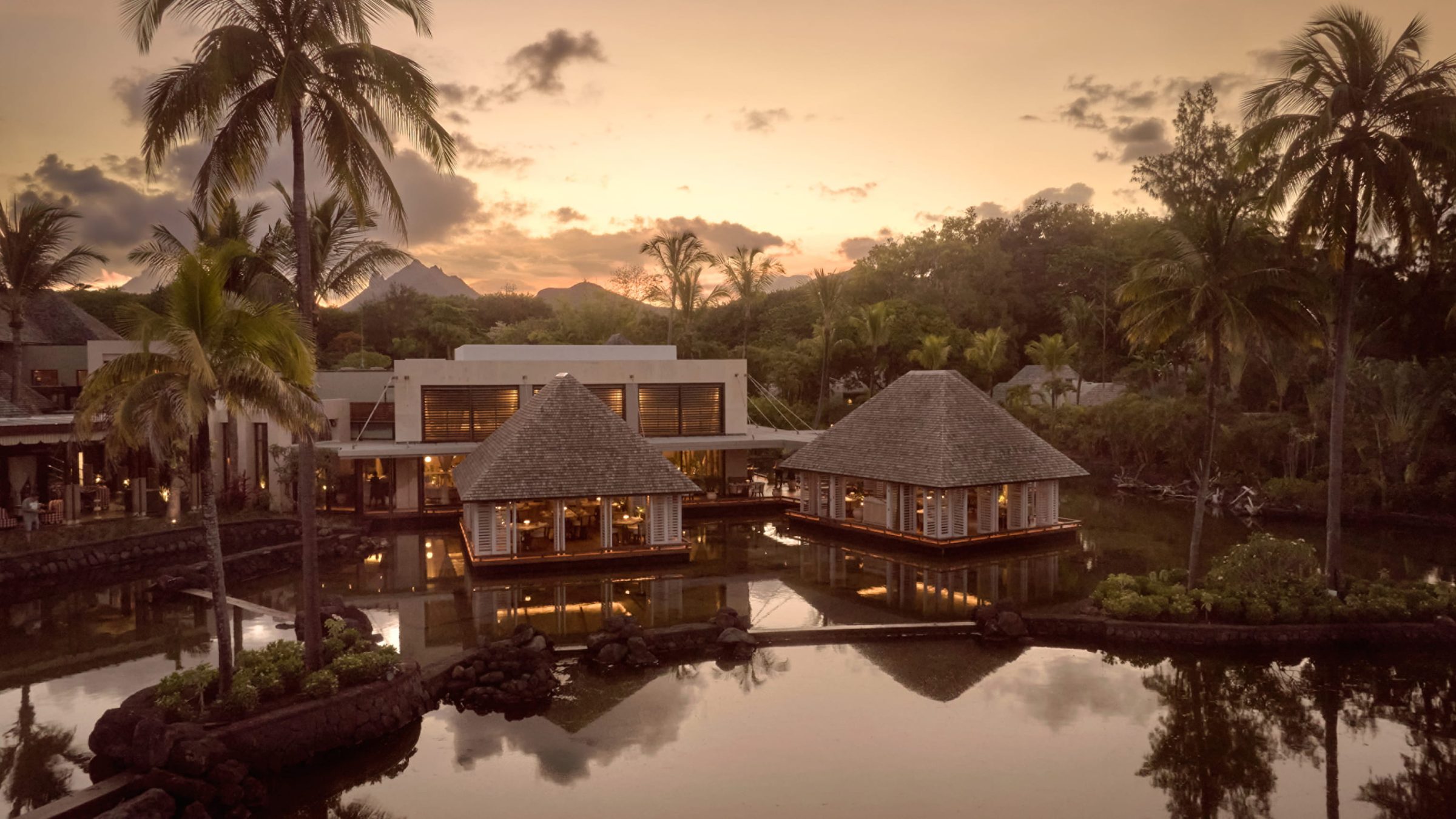 Thatched pavilions reflected in still water at sunset, Four Seasons Resort Mauritius at Anahita