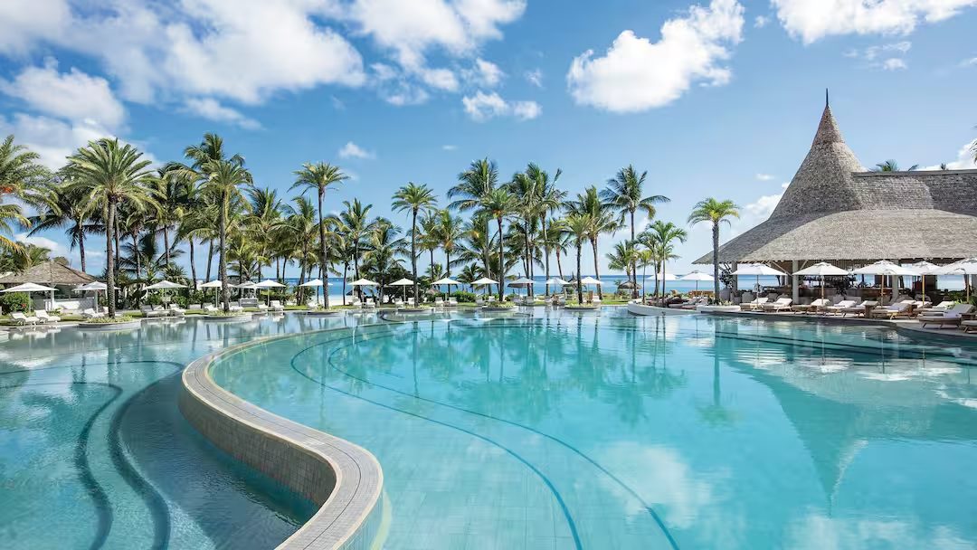Curved pool framed by palms and a thatched pavilion, LUX* Belle Mare, Mauritius