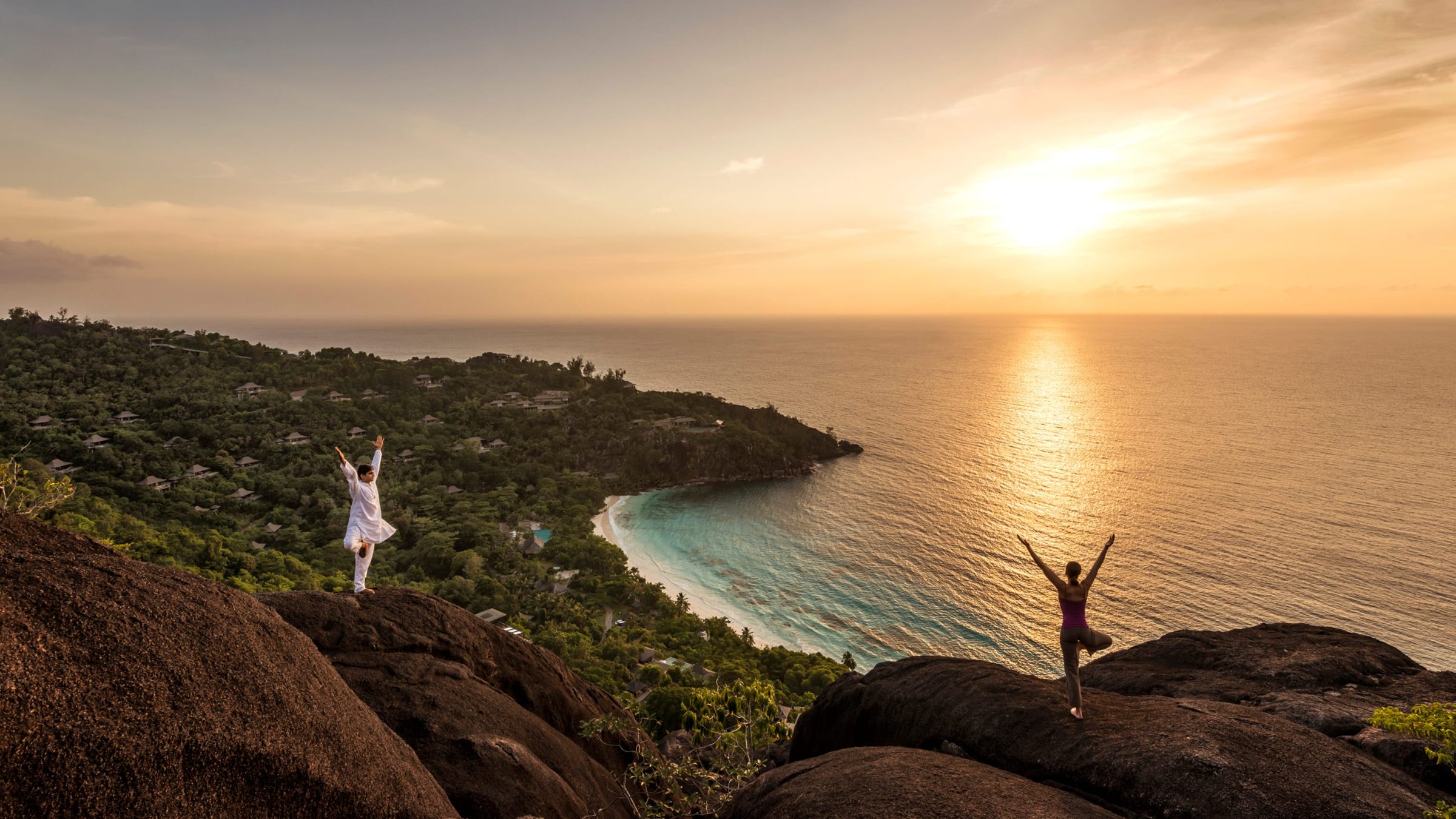 A figure watching the sun set over the sea from a granite hilltop, the Seychelles